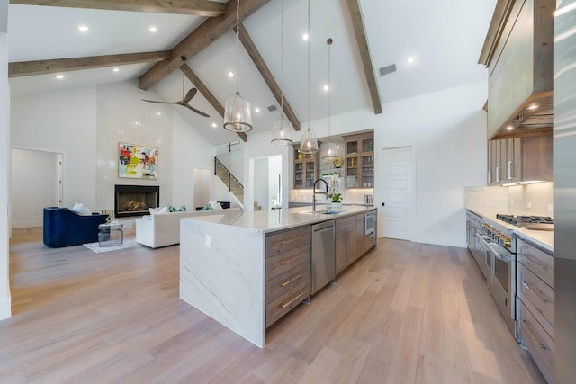 kitchen with a spacious island, a sink, stainless steel appliances, wall chimney exhaust hood, and a large fireplace