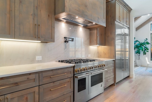 kitchen with high end appliances, light hardwood / wood-style floors, custom range hood, and backsplash