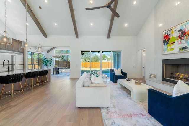 living room featuring beam ceiling, high vaulted ceiling, ceiling fan, and light wood-type flooring