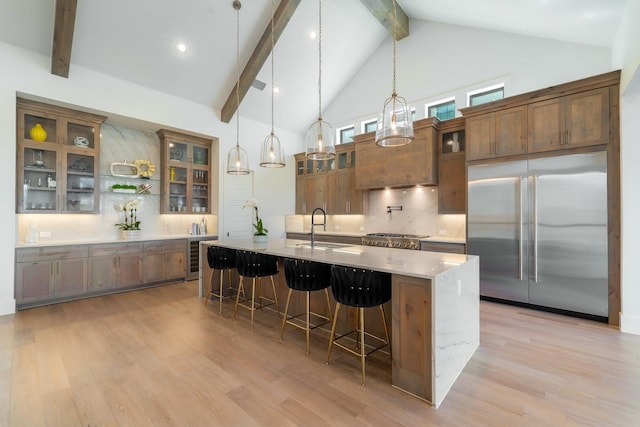 kitchen featuring a spacious island, sink, decorative light fixtures, stainless steel built in fridge, and light hardwood / wood-style floors