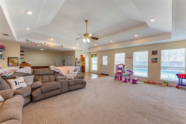 living room with plenty of natural light, light colored carpet, a raised ceiling, and ceiling fan