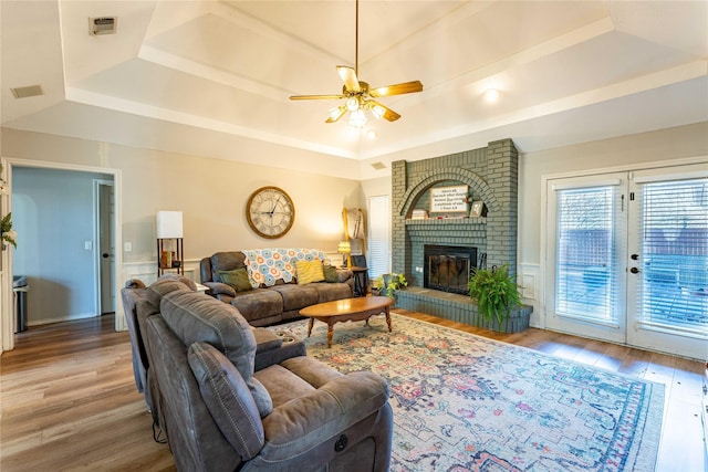 living room with hardwood / wood-style flooring, ceiling fan, a raised ceiling, and a brick fireplace