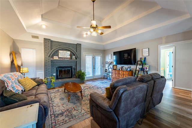 living room with wood-type flooring, ceiling fan, a fireplace, and a tray ceiling