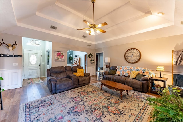 living room with ceiling fan, wood-type flooring, and a tray ceiling