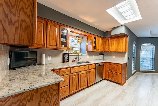 kitchen with sink, dishwasher, a skylight, tasteful backsplash, and light stone countertops