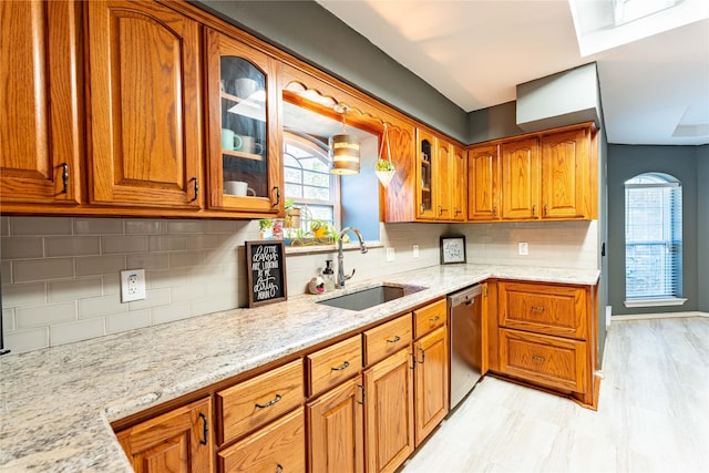 kitchen featuring tasteful backsplash, dishwasher, light stone countertops, and sink