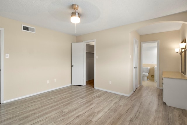 unfurnished bedroom with a walk in closet, ceiling fan, connected bathroom, light hardwood / wood-style floors, and a closet