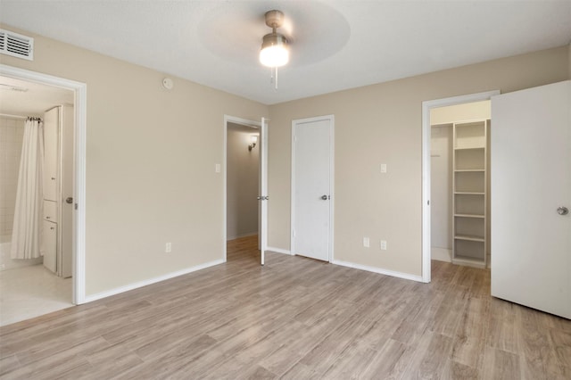 unfurnished bedroom with connected bathroom, a spacious closet, ceiling fan, light hardwood / wood-style flooring, and a closet