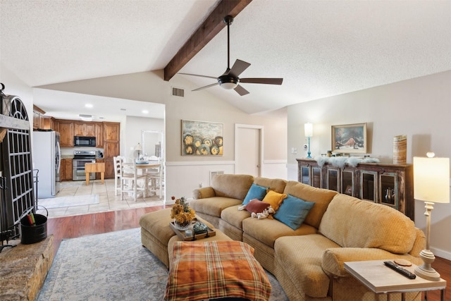 living room featuring lofted ceiling with beams, ceiling fan, light wood-type flooring, and a textured ceiling