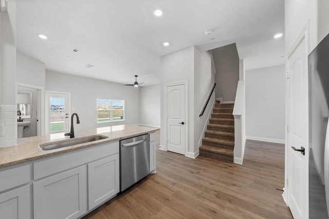 kitchen featuring ceiling fan, sink, light stone counters, stainless steel dishwasher, and light hardwood / wood-style floors