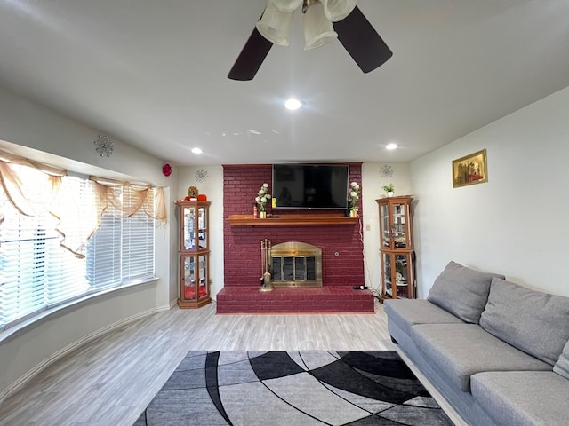 living room featuring ceiling fan, light hardwood / wood-style flooring, and a brick fireplace