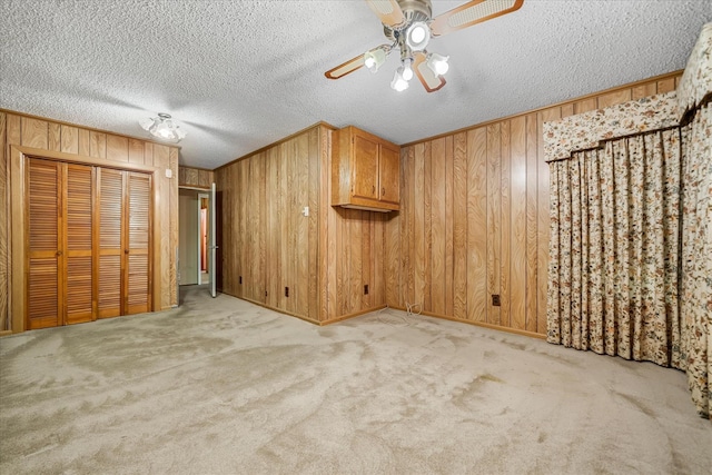 carpeted spare room with ceiling fan, a textured ceiling, and wooden walls