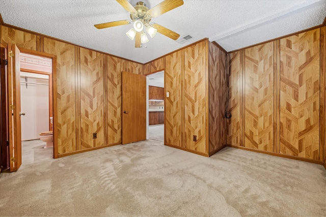 carpeted empty room featuring ceiling fan, wooden walls, a textured ceiling, and ornamental molding