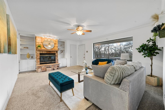 living room featuring crown molding, ceiling fan, carpet, a fireplace, and built in shelves