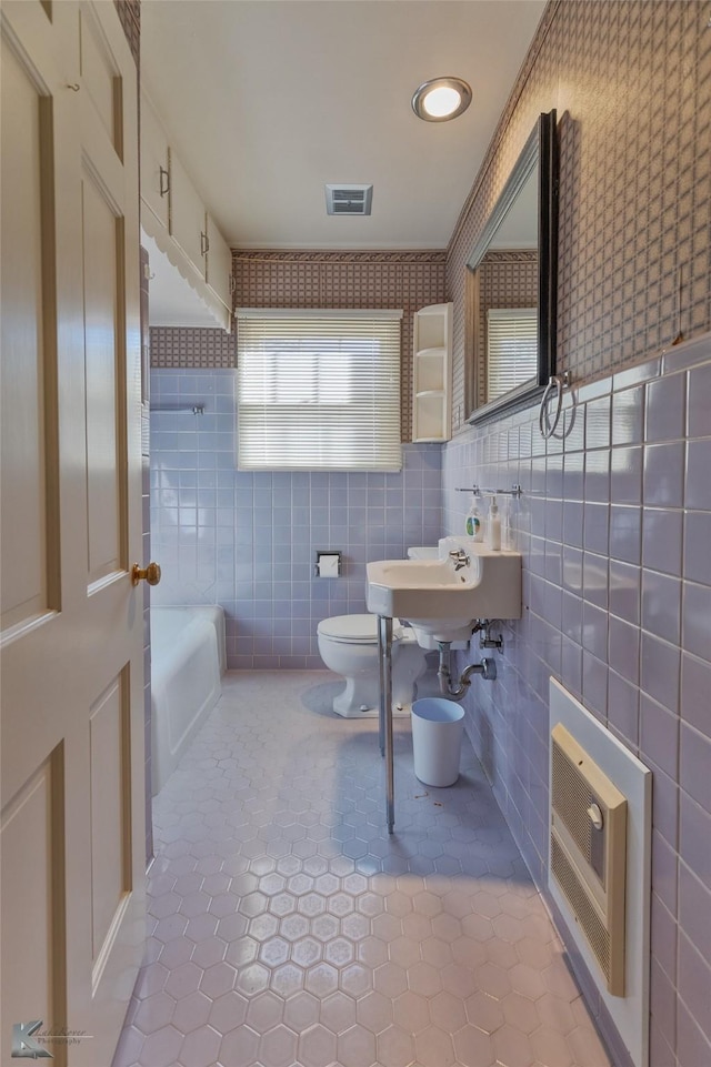 bathroom with tile patterned floors, heating unit, toilet, a bathtub, and tile walls