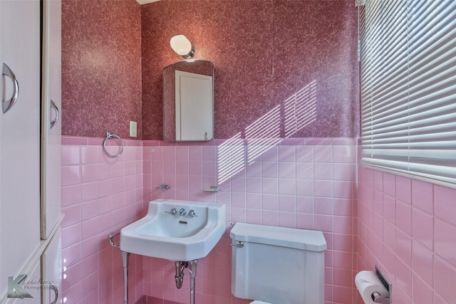 bathroom with toilet, sink, and tile walls