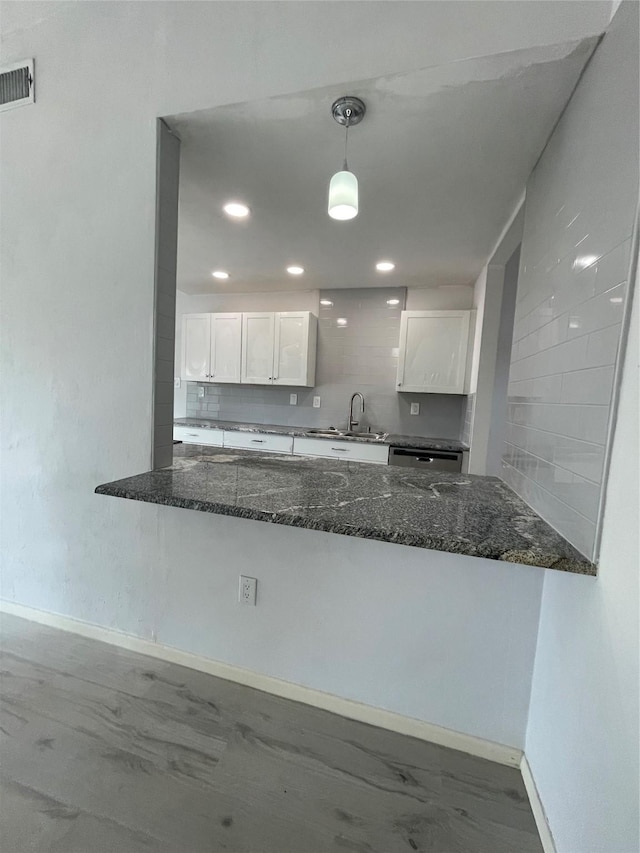 kitchen with decorative backsplash, dark stone counters, sink, white cabinets, and hanging light fixtures