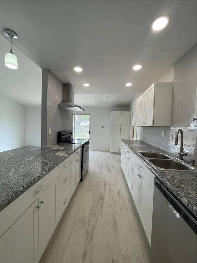 kitchen with appliances with stainless steel finishes, wall chimney range hood, sink, decorative light fixtures, and white cabinets