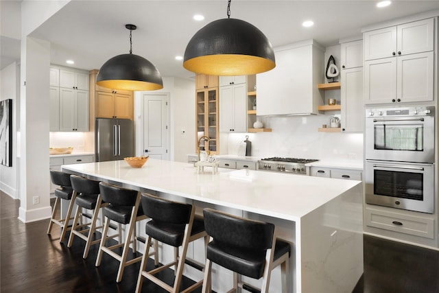 kitchen featuring white cabinets, decorative light fixtures, a kitchen island with sink, and appliances with stainless steel finishes