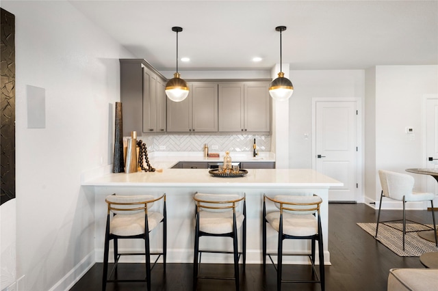 kitchen featuring gray cabinets, pendant lighting, backsplash, dark hardwood / wood-style flooring, and kitchen peninsula