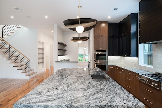 kitchen featuring hanging light fixtures, light stone counters, sink, and appliances with stainless steel finishes