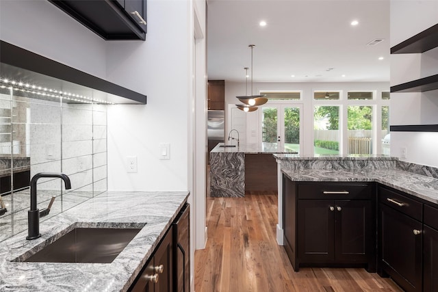 kitchen featuring sink, tasteful backsplash, light hardwood / wood-style floors, light stone counters, and dark brown cabinetry