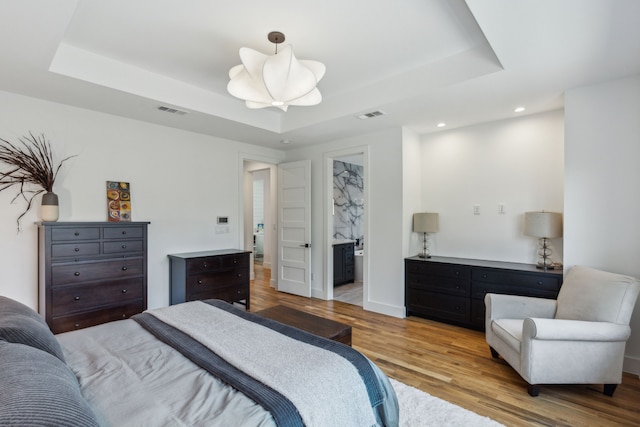 bedroom featuring a tray ceiling, ensuite bathroom, and light hardwood / wood-style floors