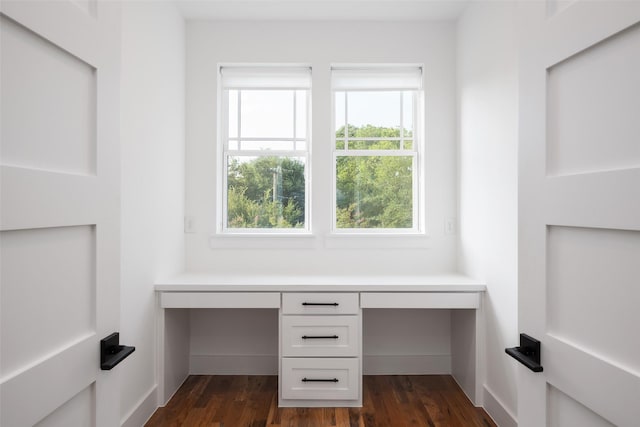 unfurnished office featuring built in desk and dark hardwood / wood-style floors