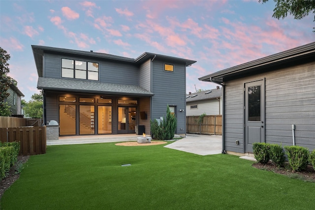 back house at dusk featuring a lawn and a patio