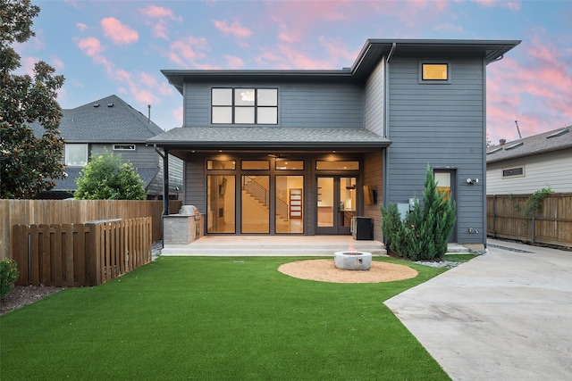 back house at dusk featuring a patio area and a lawn