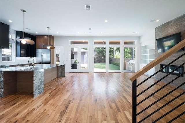 kitchen featuring stainless steel built in fridge, sink, decorative light fixtures, light hardwood / wood-style floors, and light stone counters