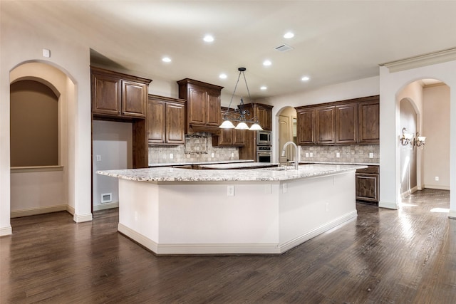 kitchen with light stone countertops, appliances with stainless steel finishes, a kitchen island with sink, and dark hardwood / wood-style floors