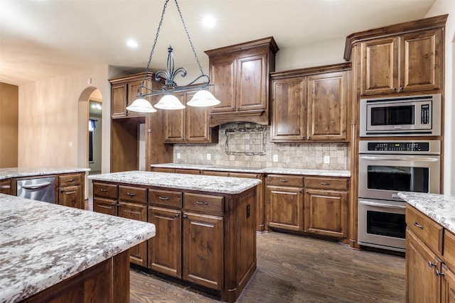 kitchen with pendant lighting, appliances with stainless steel finishes, a kitchen island, dark hardwood / wood-style flooring, and decorative backsplash