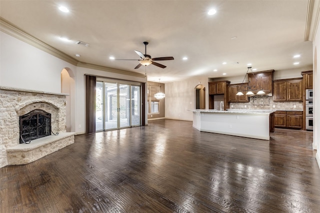 unfurnished living room with a stone fireplace, ceiling fan, crown molding, and dark hardwood / wood-style floors