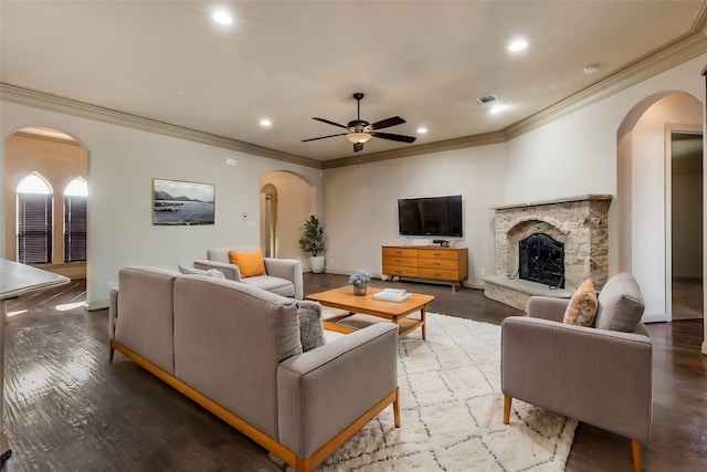 living room featuring ceiling fan, a stone fireplace, and ornamental molding