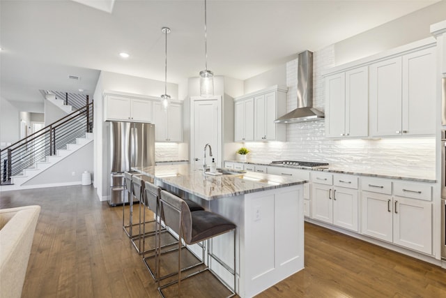 kitchen with a center island with sink, white cabinetry, wall chimney range hood, and sink