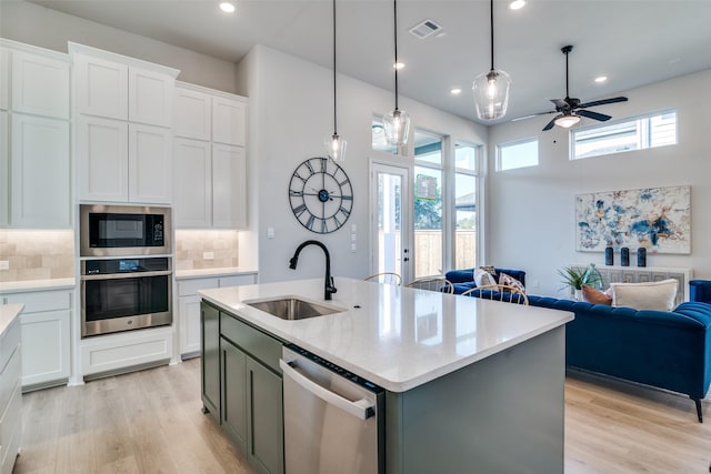 kitchen featuring a center island with sink, sink, tasteful backsplash, white cabinetry, and stainless steel appliances