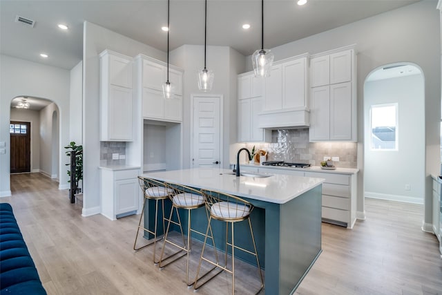 kitchen featuring backsplash, a kitchen island with sink, sink, and white cabinets