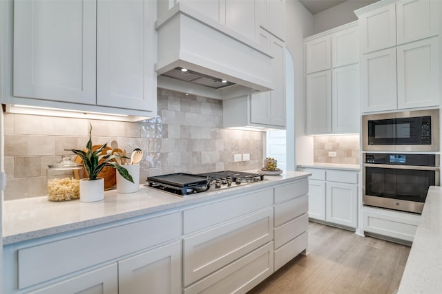 kitchen with light stone countertops, appliances with stainless steel finishes, backsplash, custom range hood, and white cabinetry