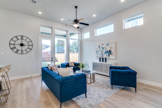 living room featuring ceiling fan, light hardwood / wood-style floors, and a towering ceiling