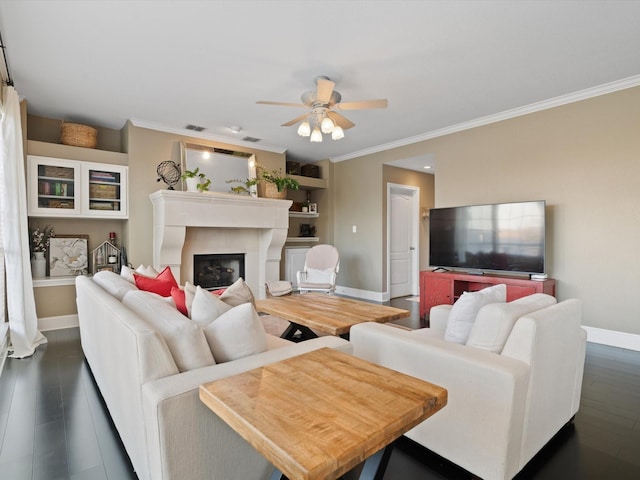 living room with built in shelves, crown molding, ceiling fan, and dark wood-type flooring