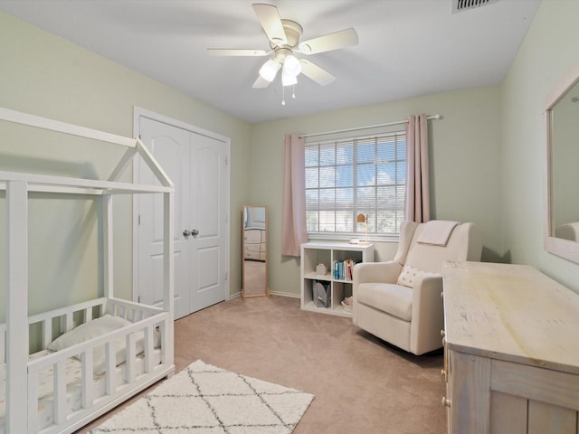 bedroom with ceiling fan, a closet, light colored carpet, and a crib