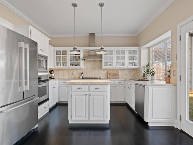 kitchen featuring wall chimney exhaust hood, stainless steel appliances, sink, decorative light fixtures, and white cabinets