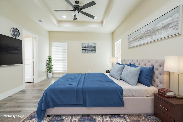 bedroom with hardwood / wood-style flooring, ceiling fan, and a raised ceiling