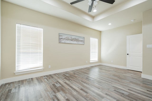 empty room with a raised ceiling, ceiling fan, light hardwood / wood-style flooring, and plenty of natural light