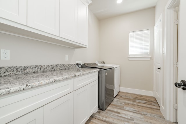 laundry room featuring light wood-type flooring, washing machine and dryer, and cabinets