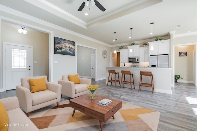 living room featuring sink, ceiling fan, ornamental molding, a tray ceiling, and light hardwood / wood-style floors