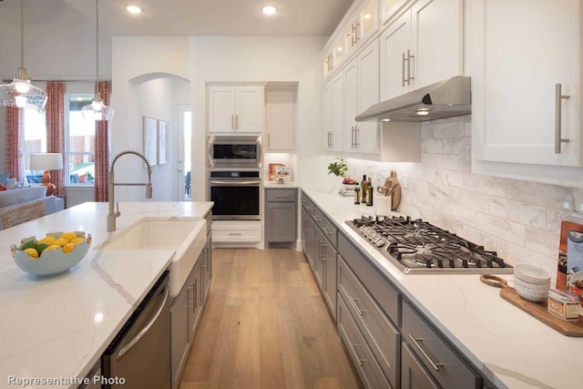 kitchen with white cabinetry, appliances with stainless steel finishes, light stone counters, and hanging light fixtures