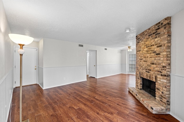 unfurnished living room with ceiling fan, dark hardwood / wood-style flooring, a textured ceiling, and a brick fireplace