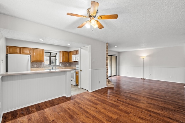 kitchen with kitchen peninsula, light wood-type flooring, tasteful backsplash, white appliances, and ceiling fan